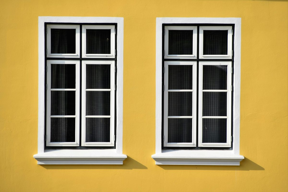 Deux fenêtres à petits carreaux encadrées de blanc sur une façade jaune